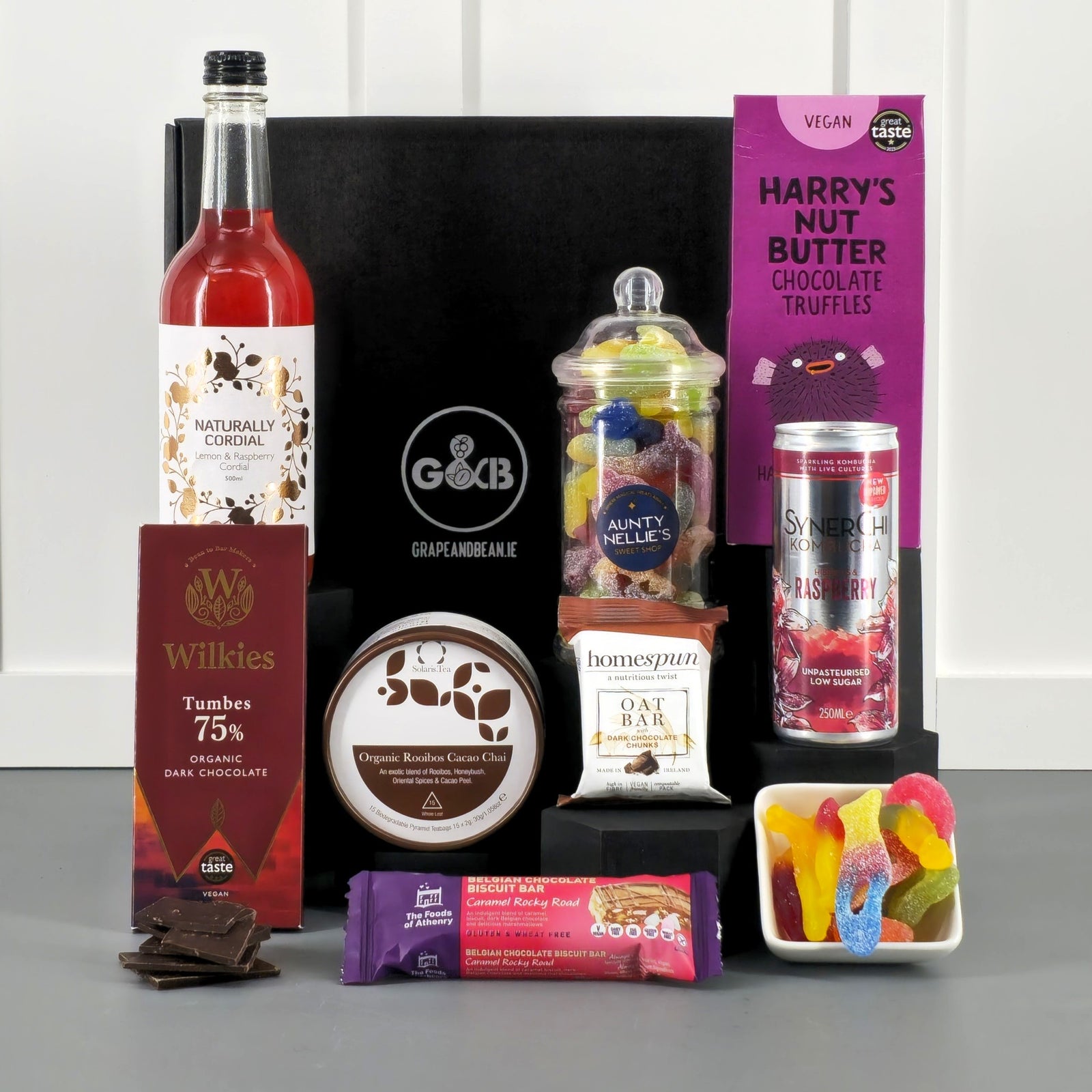 Assorted snacks and drinks including cordial, truffles, jellies, chocolate, tea bags, kombucha in a black gift box