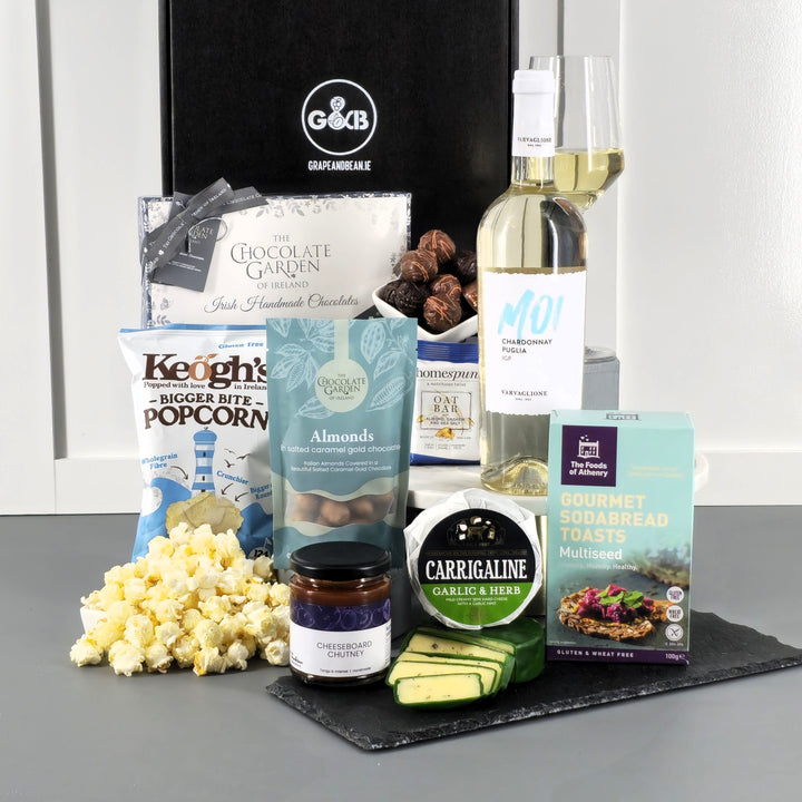 Assorted gourmet food items including popcorn, chocolate, cheese, chutney and white wine in a black gift box