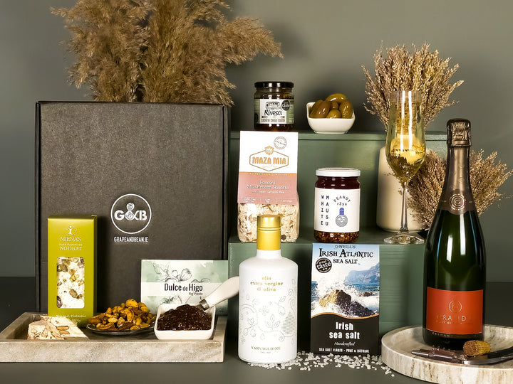 Gourmet gift set with items including a bottle of champagne, a jar of honey, and a box of chocolates on a gray surface.